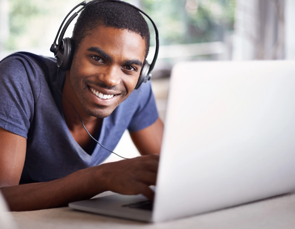 Student wearing headphones smiling while studying on a laptop