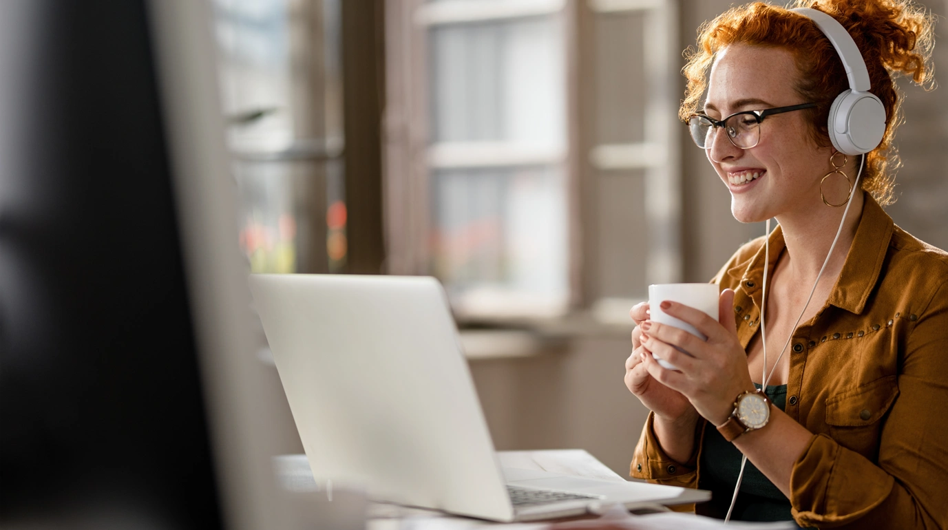 Student with headphones and a cup of coffee joining an online class on a laptop